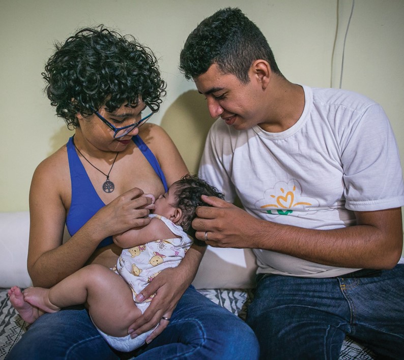 Mãe amamenta filha e pai observa