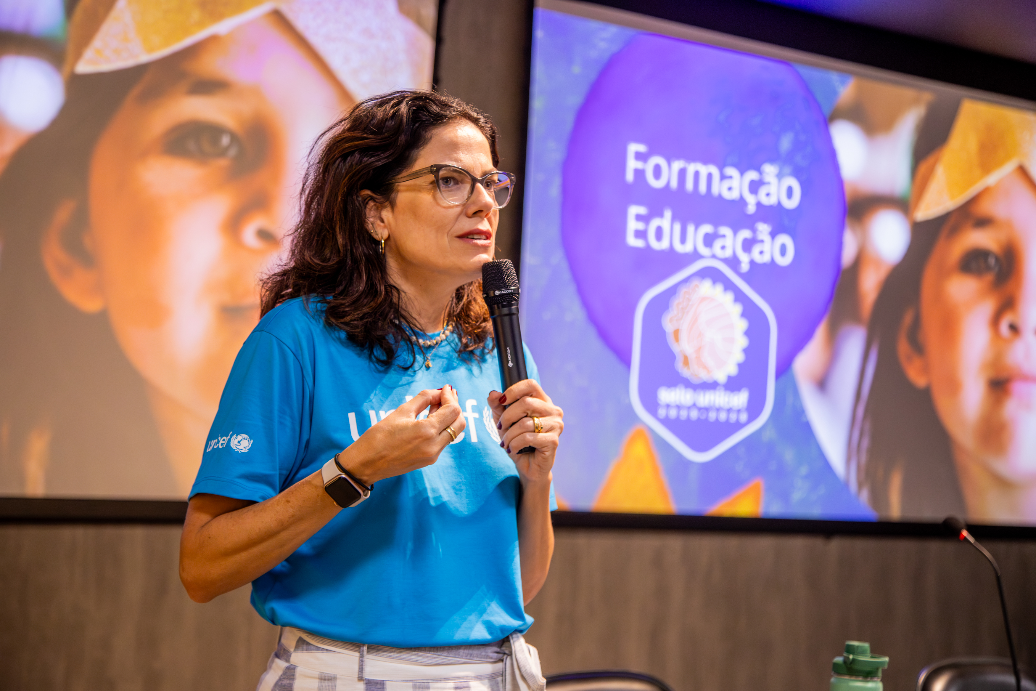Oficial de educaÃ§Ã£o do Unicef, JÃºlia Ribeiro, segura o microfone enquanto palestra