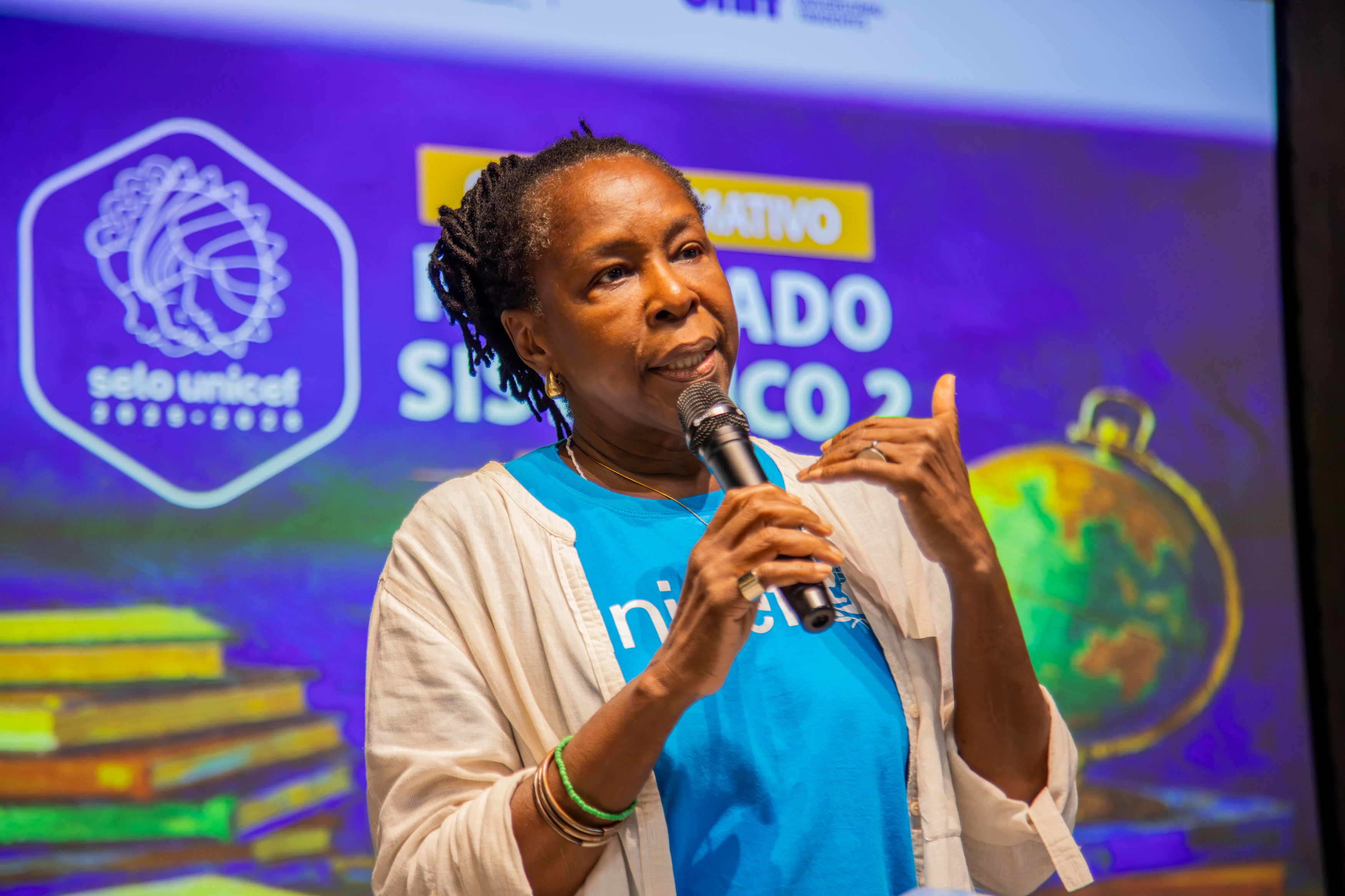Chefe do escritÃ³rio do UNICEF, Helena Oliveira, segura o microfone e palestra na formaÃ§Ã£o