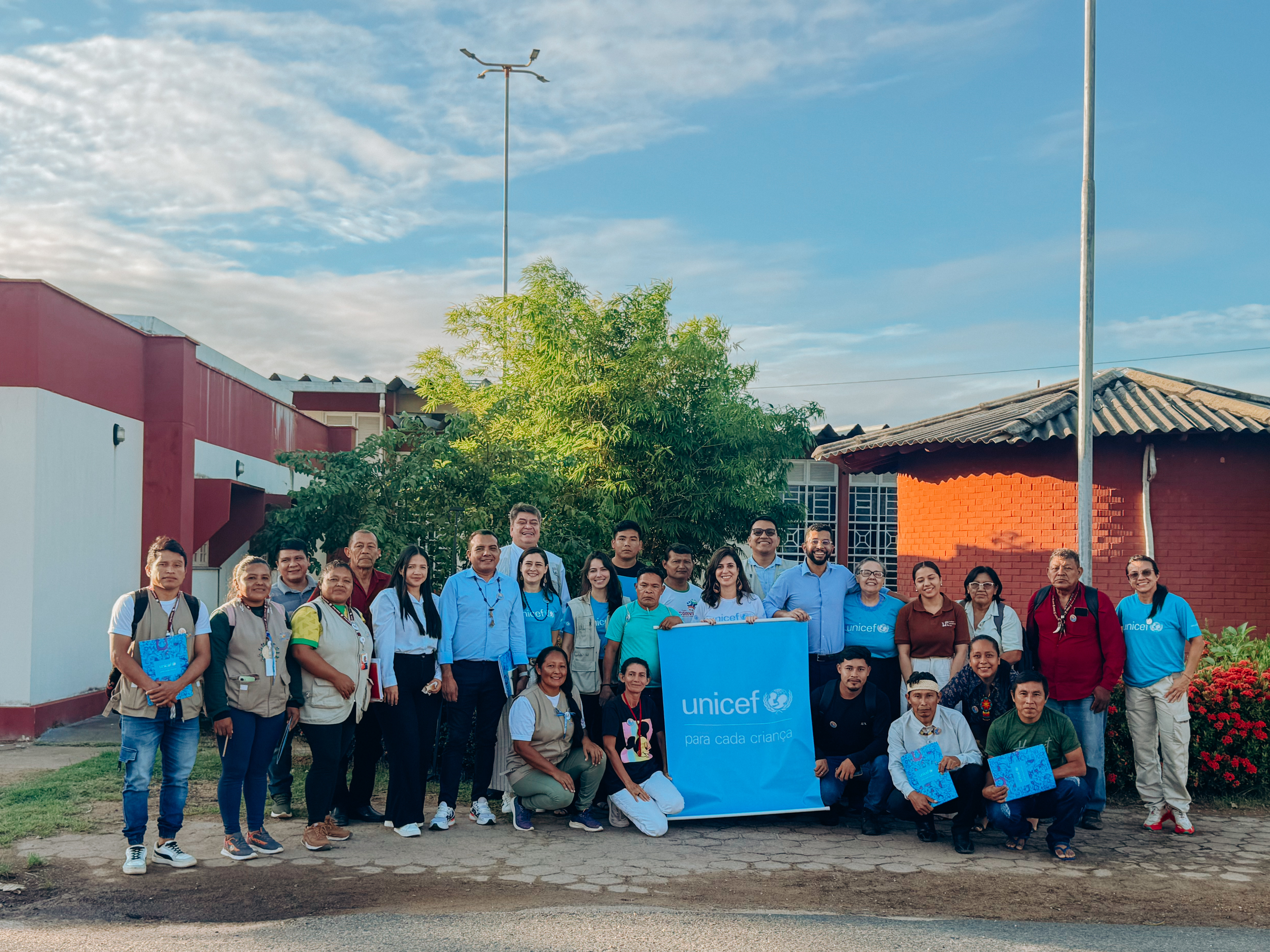 organizaÃ§Ãµes indÃ­genas e profissionais do UNICEF pousam para a foto ao ar livre com o logo do UNICEF