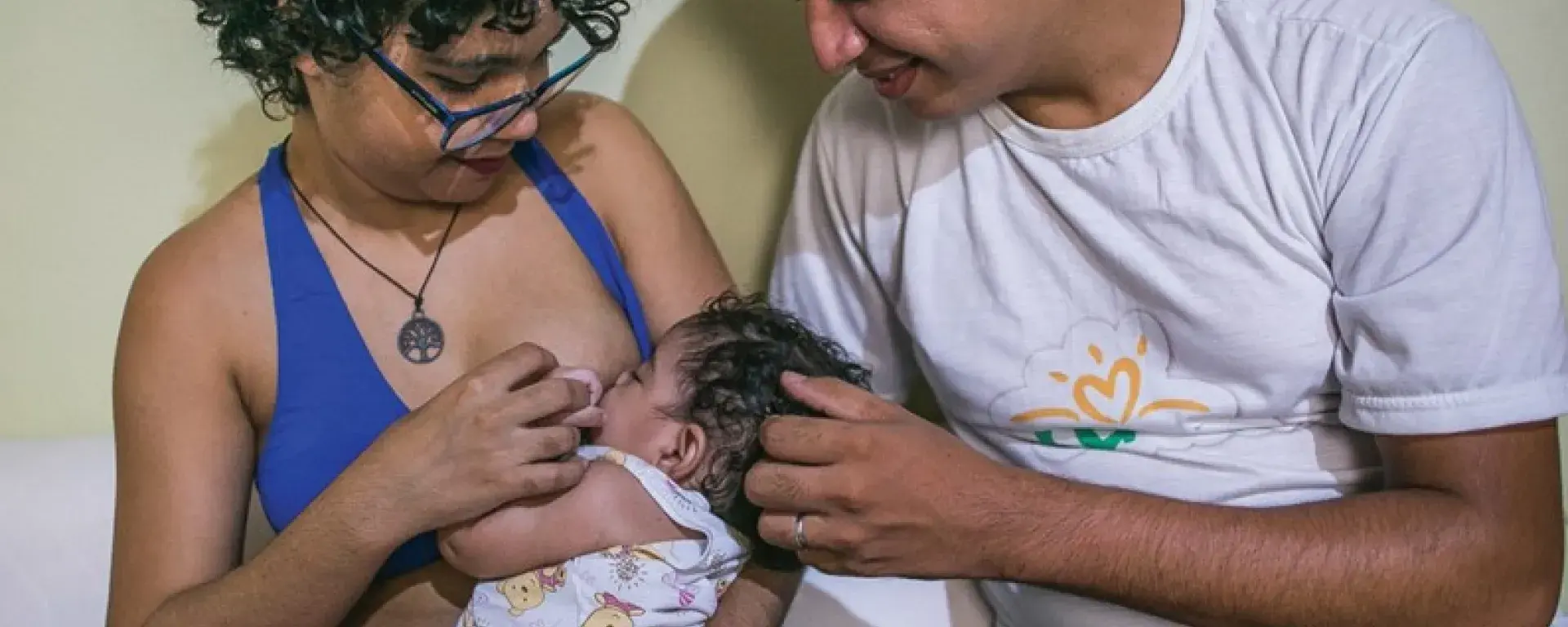 Mãe amamenta filha e pai observa