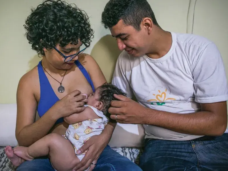 Mãe amamenta filha e pai observa