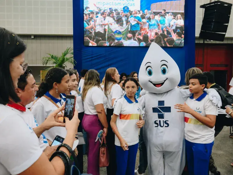 Zé Gotinha com adolescentes do lado sorrindo para foto.