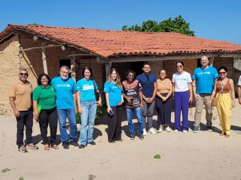 Grupo do UNICEF pousa para foto na frente de uma casa de barro