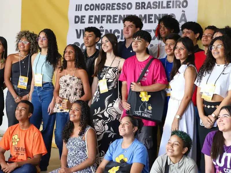 Grupo de adolescentes possam para foto ao fundo banner do evento