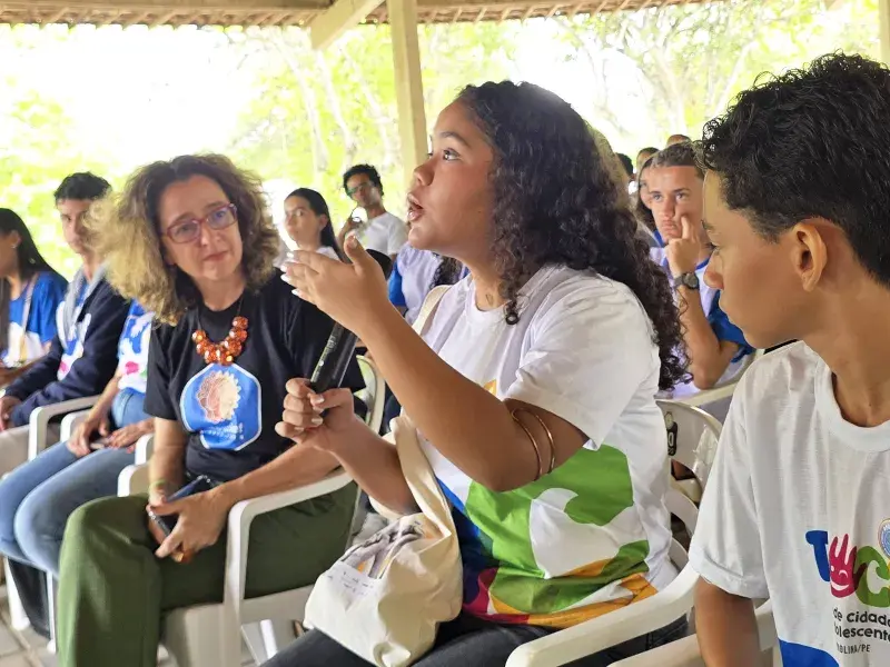 menina adolescente fala com microfone em meio a uma reunião