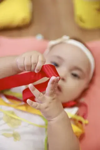 Bebê brinca com laço de fita vermelho