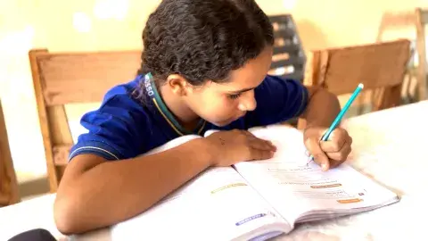 Adolescente negra fardada escrevendo em um livro
