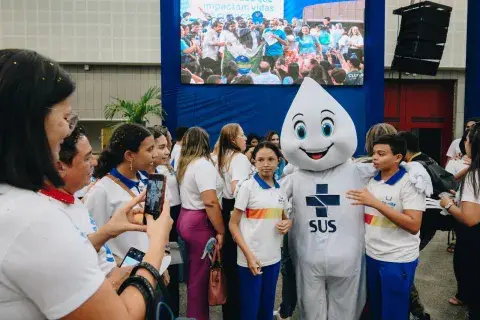 Zé Gotinha com adolescentes do lado sorrindo para foto.