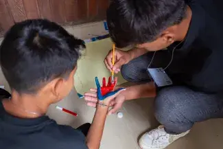 Dois garotos, um pintando a mão de outro com tintas azul e vermelha