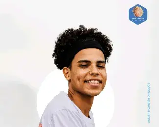 Adolescente negro de pele clara sorri para a câmera, em fundo branco