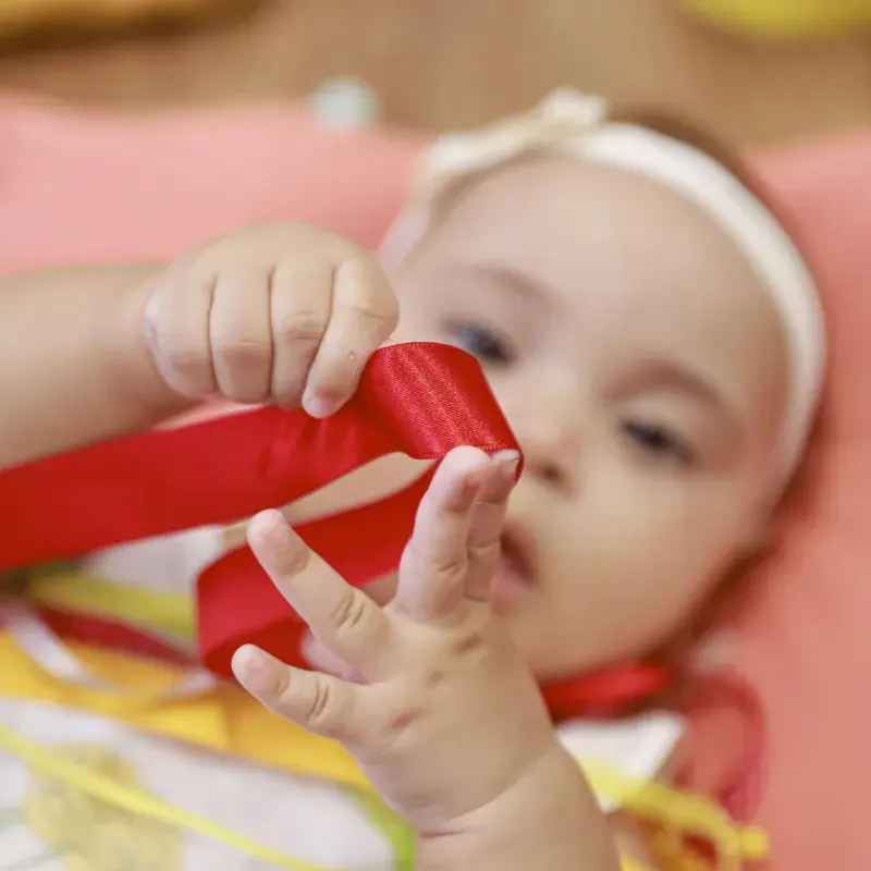 Bebê brinca com laço de fita vermelho