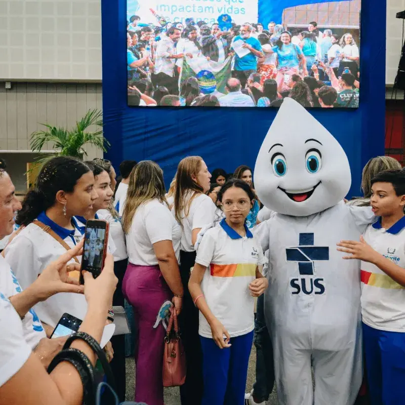 Zé Gotinha com adolescentes do lado sorrindo para foto.