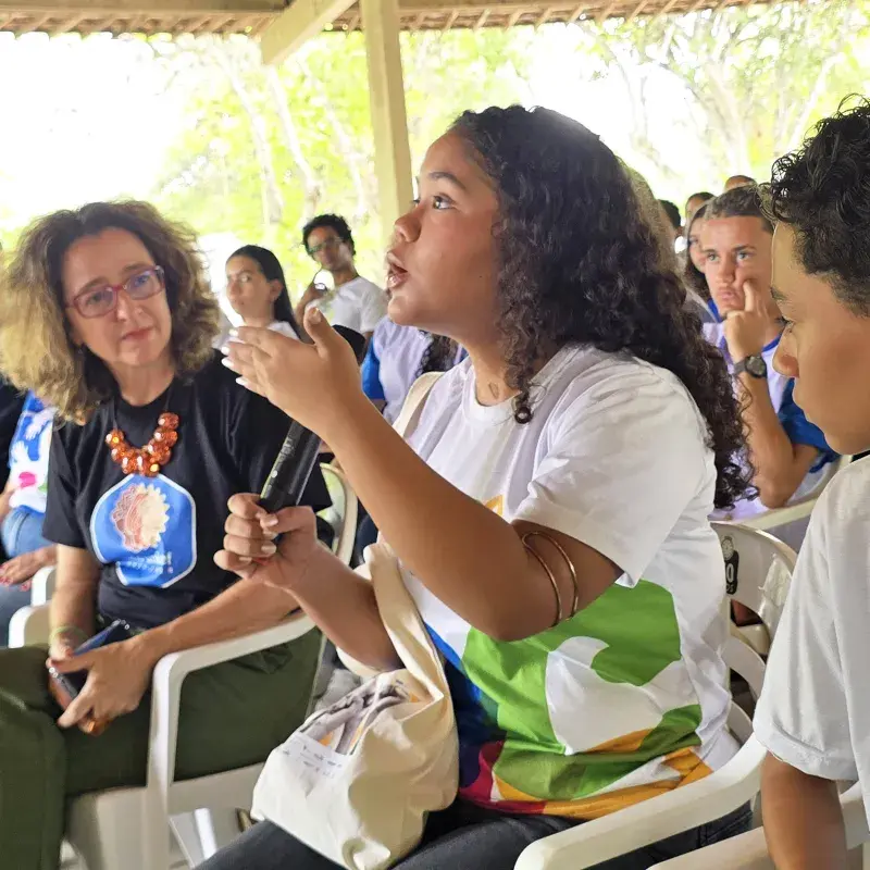 menina adolescente fala com microfone em meio a uma reunião